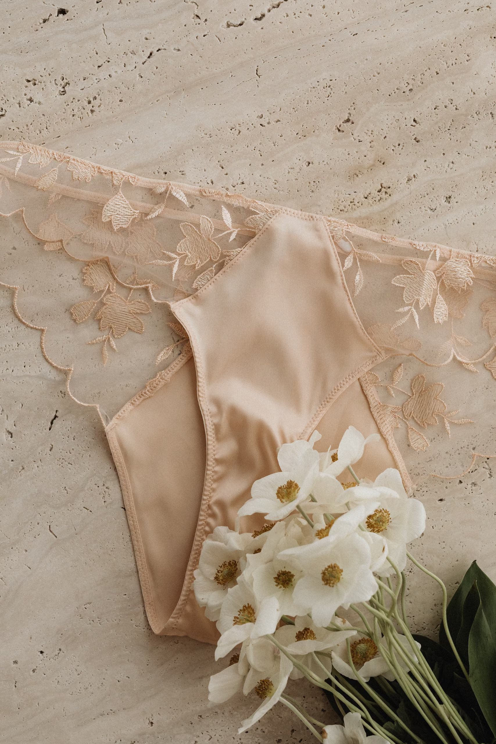 Une culotte en dentelle beige, un bouquet de fleurs blanches posé dessus.